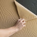 Hand applying brown paper to a textured surface