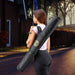 Woman carrying a long black bag with a logo on a residential street.