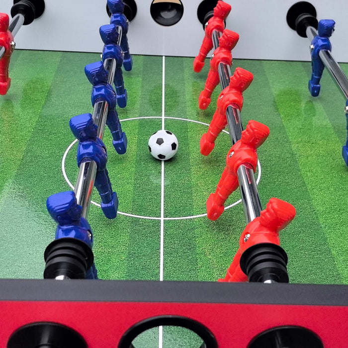 Close-up of a foosball table with red and blue player figures around a black and white ball.