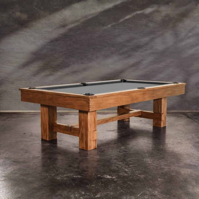 Wooden pool table with a gray felt surface on a dark concrete floor.