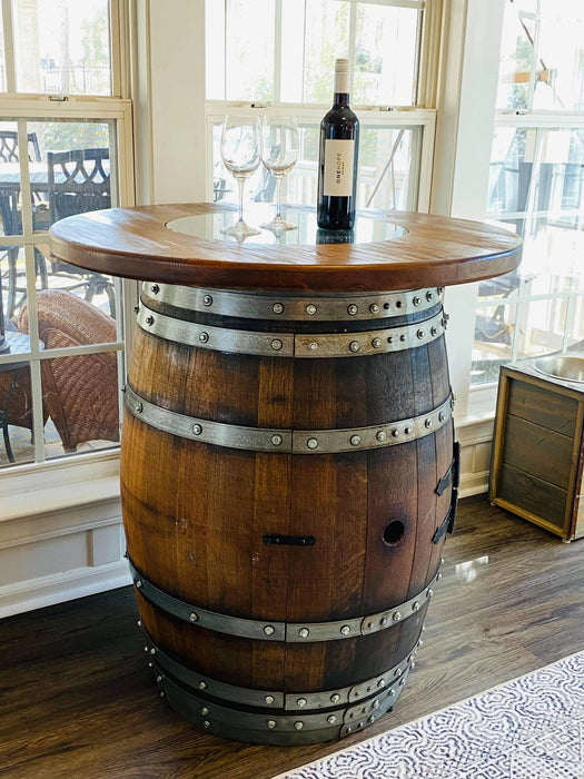 Wooden barrel table with a bottle of wine and glasses in a room with large windows.