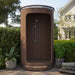 Wooden outdoor shower enclosure in a garden setting with plants and a house in the background.