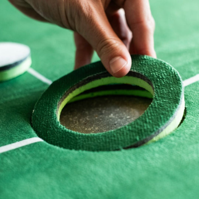 Close-up of a hand holding a green and black sanding disc on a green surface.