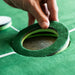 Close-up of a hand holding a green and black sanding disc on a green surface.