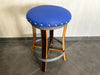 Bar stool with blue cushioned seat and wooden legs on a tiled floor.