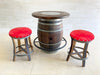 Barrel table with two red cushioned stools on a light tiled floor.