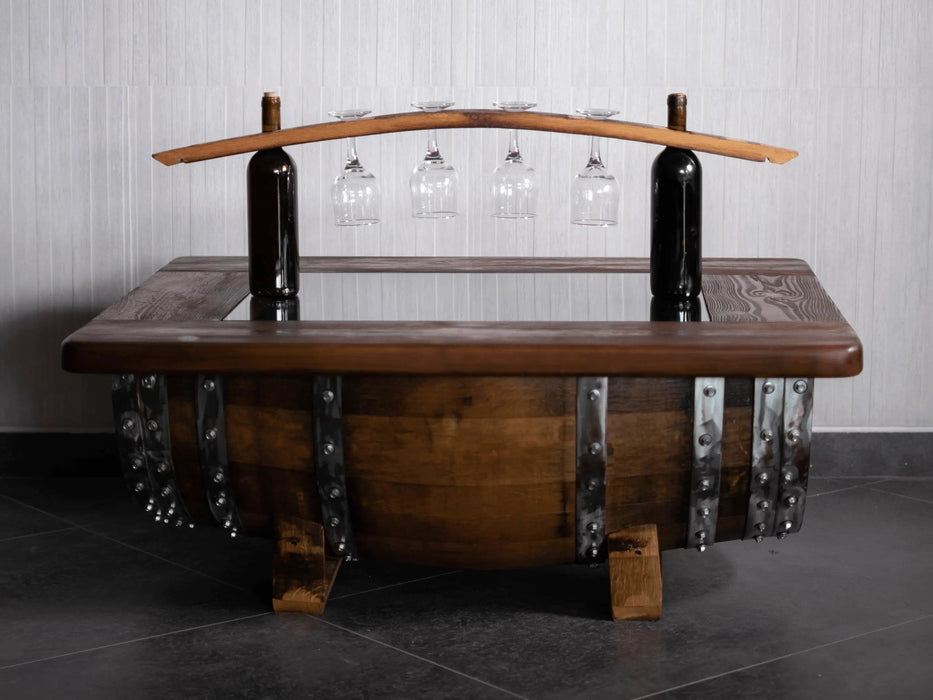 Wooden barrel table with wine bottles and glasses on a tiled floor.
