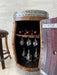 Wooden barrel with wine bottles and glasses inside, against a light-colored wall.